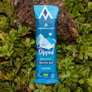 Moonvalley ekologisk proteinbar med kakao och chokladöverdrag, fotograferad i naturlig utomhusmiljö.