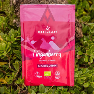 Moonvalley ekologisk sportdryck med smak av lingon i pulverform, fotograferad i naturlig utomhusmiljö.
