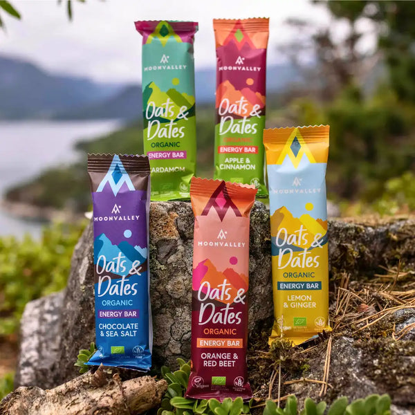 Moonvalleys ekologiska energibars i flera smaker placerade på klippor i naturskön utomhusmiljö.