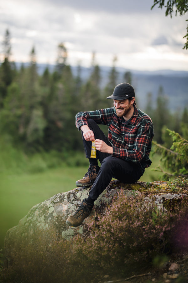 Person som sitter utomhus i naturen och äter en Moonvalley energibar.