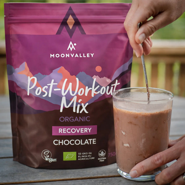 Ett glas med färdigblandad chokladdryck från Moonvalley Post-Workout Mix rörs om med en sked.